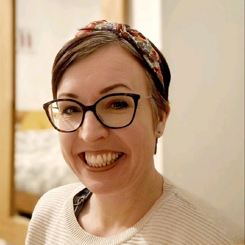 A picture of Annie Turnbull from Oxfam, she is wearing dark rimmed glasses, has short brunett hair with a floral headband. 